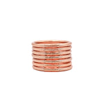 Pila de pulseras lisas en tono cobre sobre fondo blanco.