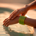 Pulseras verdes en una muñeca junto al agua al atardecer.