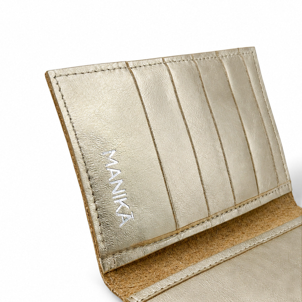 Detalle de los tarjeteros y el logo MANIKĀ grabado en una cartera de piel vacuna metalizada dorada